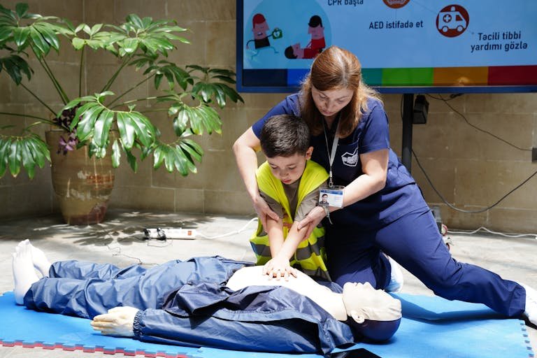Nurse guides child in CPR training using a dummy indoors.